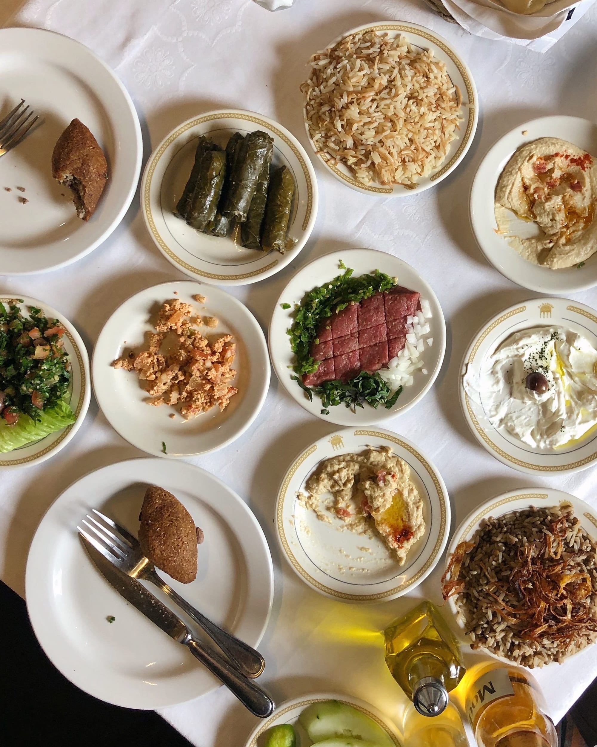 A table set with many small Mediterranean mezze dishes, including stuffed vine leaves, hummus and salads