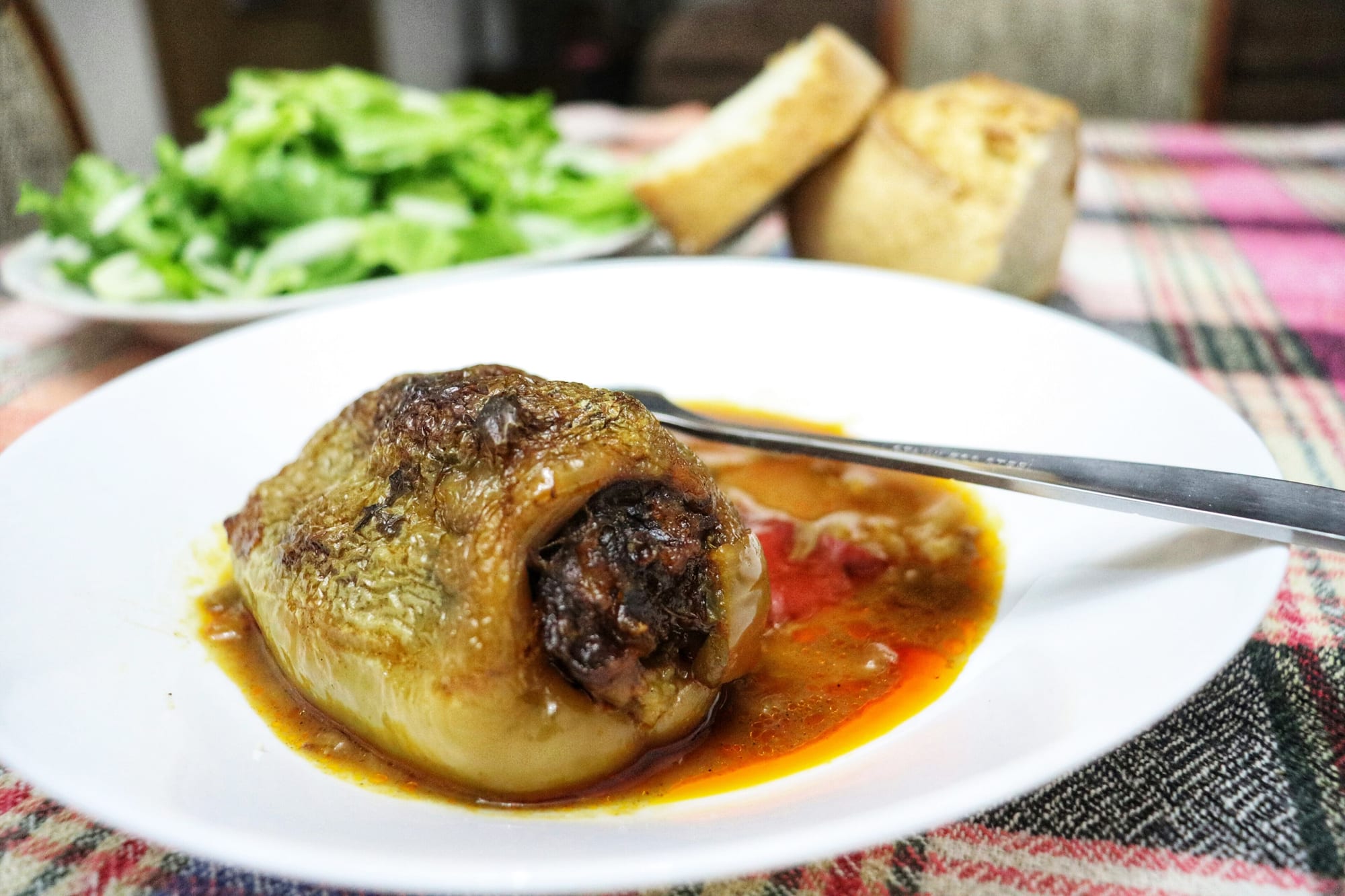 A baked pepper stuffed with minced meat and rice, served on a white plate with its cooking juices