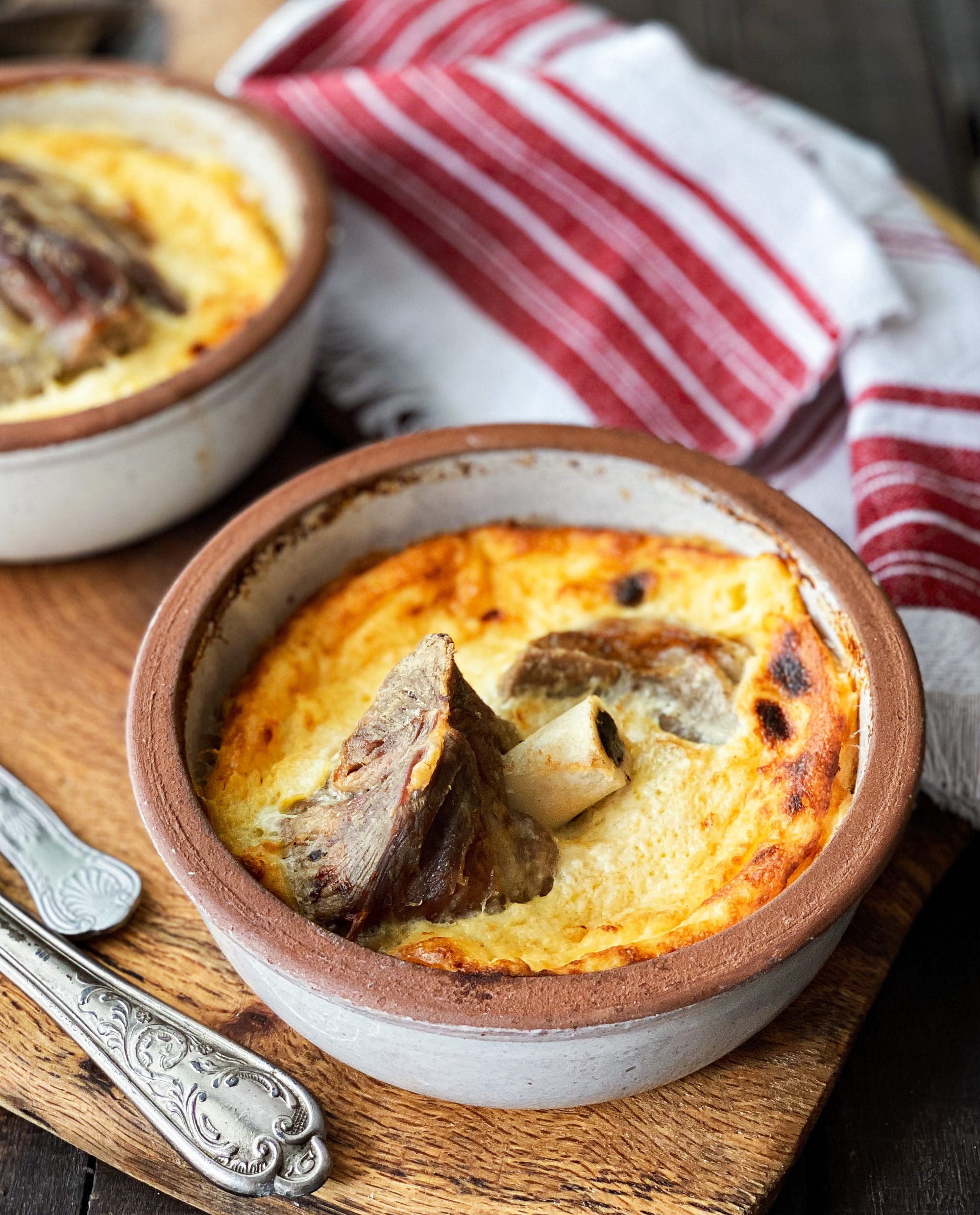 Tavë kosi in a clay dish — lamb baked under a golden, puffed yogurt and egg topping