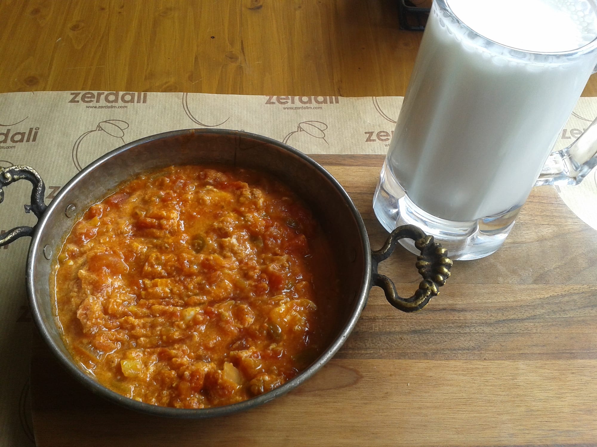 Menemen — eggs scrambled into tomatoes and peppers — in a small copper pan next to a glass of ayran